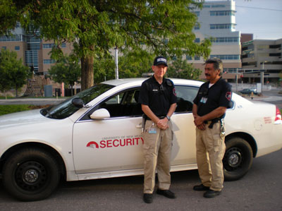 Two security officers stand next to vehicle